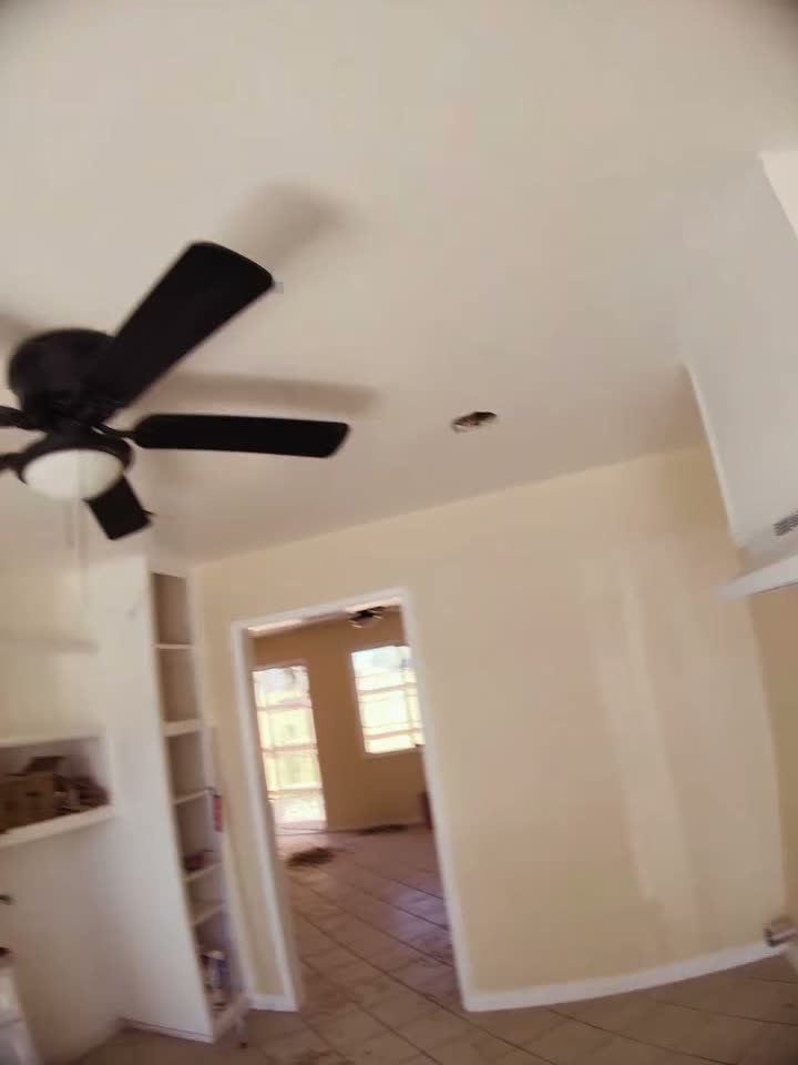 A new black ceiling fan with a light kit installed in a freshly painted room, recessed lights in the ceiling behind it.