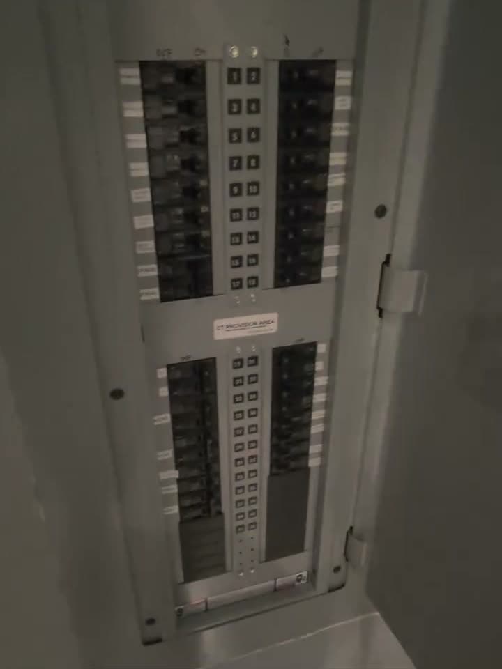 A commercial electrical panel with its dead front on, two columns of breakers set in a painted wall.