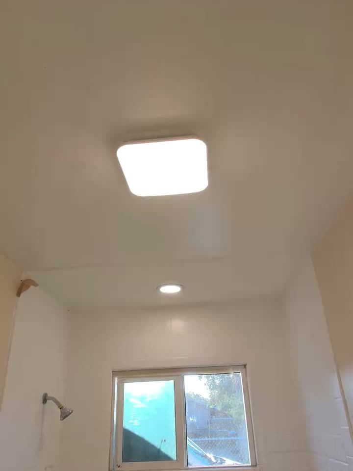 A finished room with a new square LED ceiling light and a recessed can, both switched on.