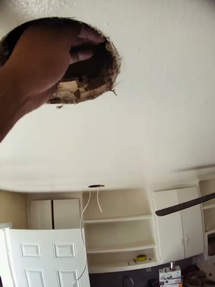 An electrician's hand at a freshly cut ceiling hole, pulling the new wire through for a fixture.