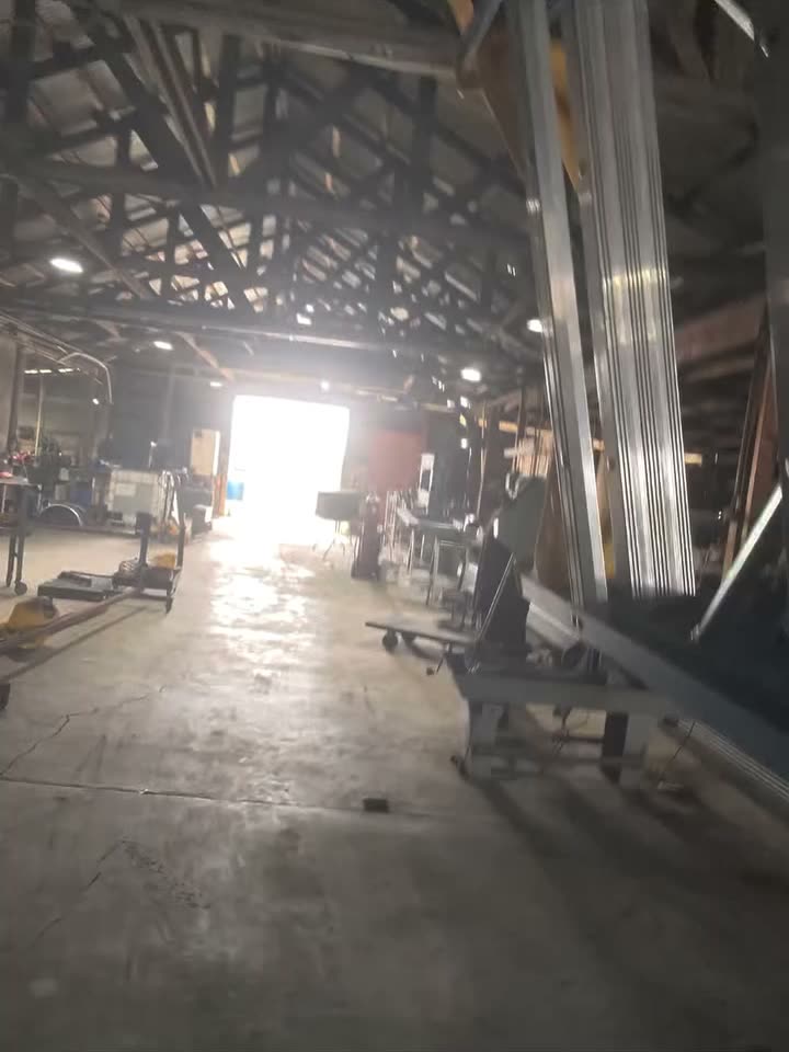 Looking down the length of an open-sided warehouse shed, daylight at the far end, before the work starts.